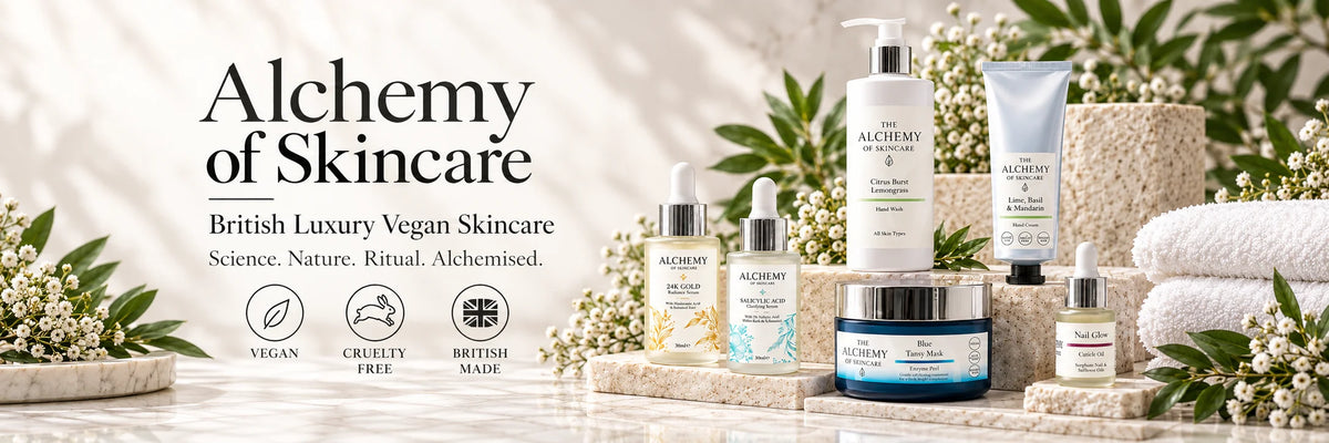 A promotional banner for Alchemy of Skincare, showcasing a collection of British Luxury Vegan Skincare products including bottles, jars, and tubes arranged on a stone surface with white flowers and green leaves.