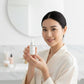 Woman holding a skincare bottle in a bathroom setting