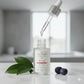 Skincare serum bottle with dropper and leaves on a neutral background