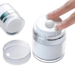 A clear cylindrical cosmetic jar with a white screw-top lid and a small white central button, shown with a hand pressing that button. A separate clear lid and another jar are visible on a plain white background.