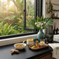 Table with skincare products and a vase of flowers by a window with a garden view